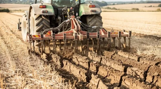 Tracteur tirant un décompacteur à dents multiples travaillant un champ agricole, les dents pénétrant visiblement le sol compacté